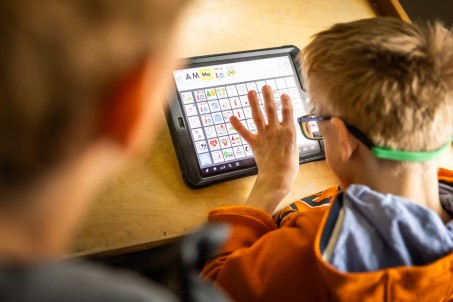 Blick über die Schulter eines Schülers auf die elektronische Kommunikationshilfe