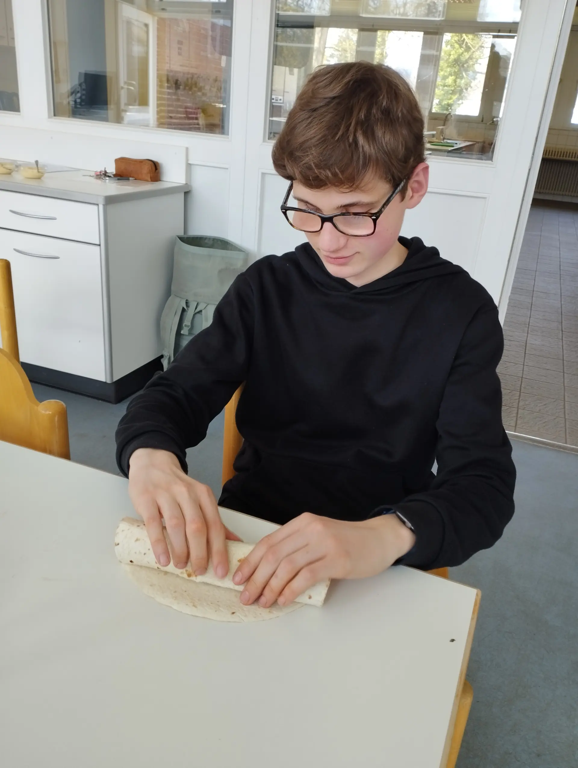 Ein Schüler sitzt am Tisch und rollt seinen Wrap