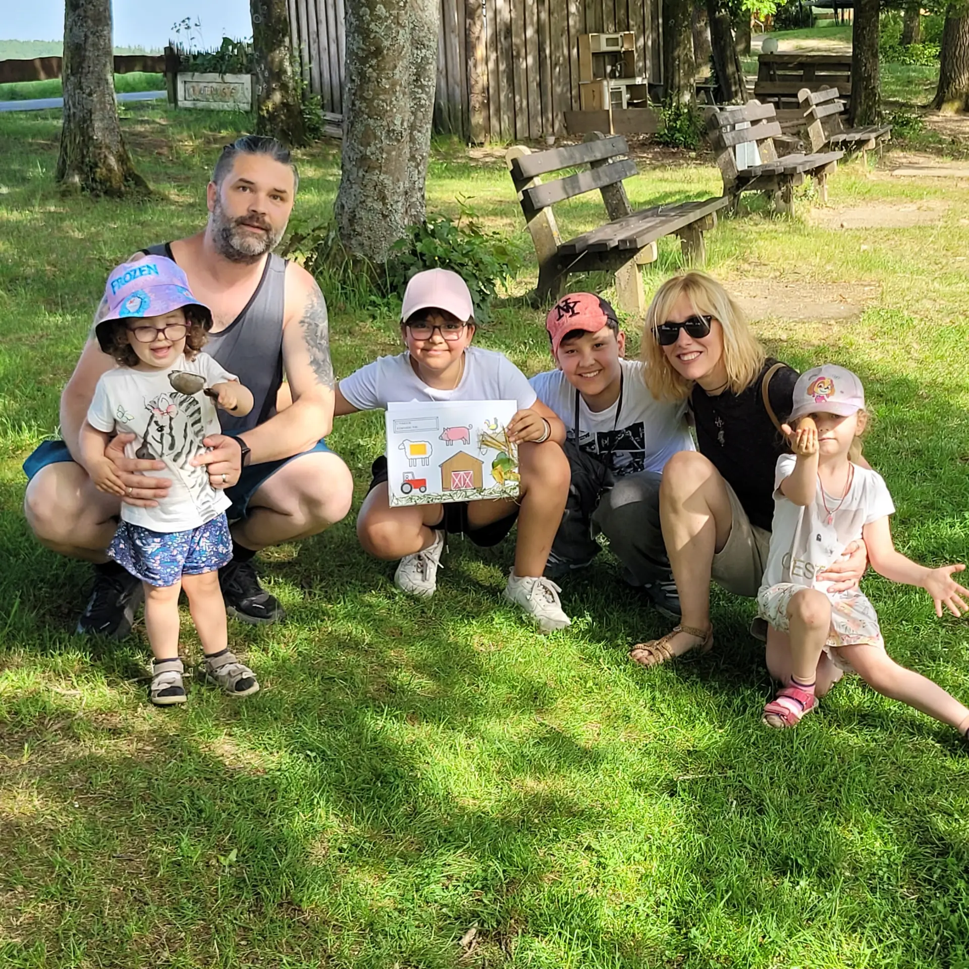 Familienfoto der Familie Müller auf einer Wiese. Die Kinder halten die gefundenen Gegenstände und die tastbare Karte in den Händen.