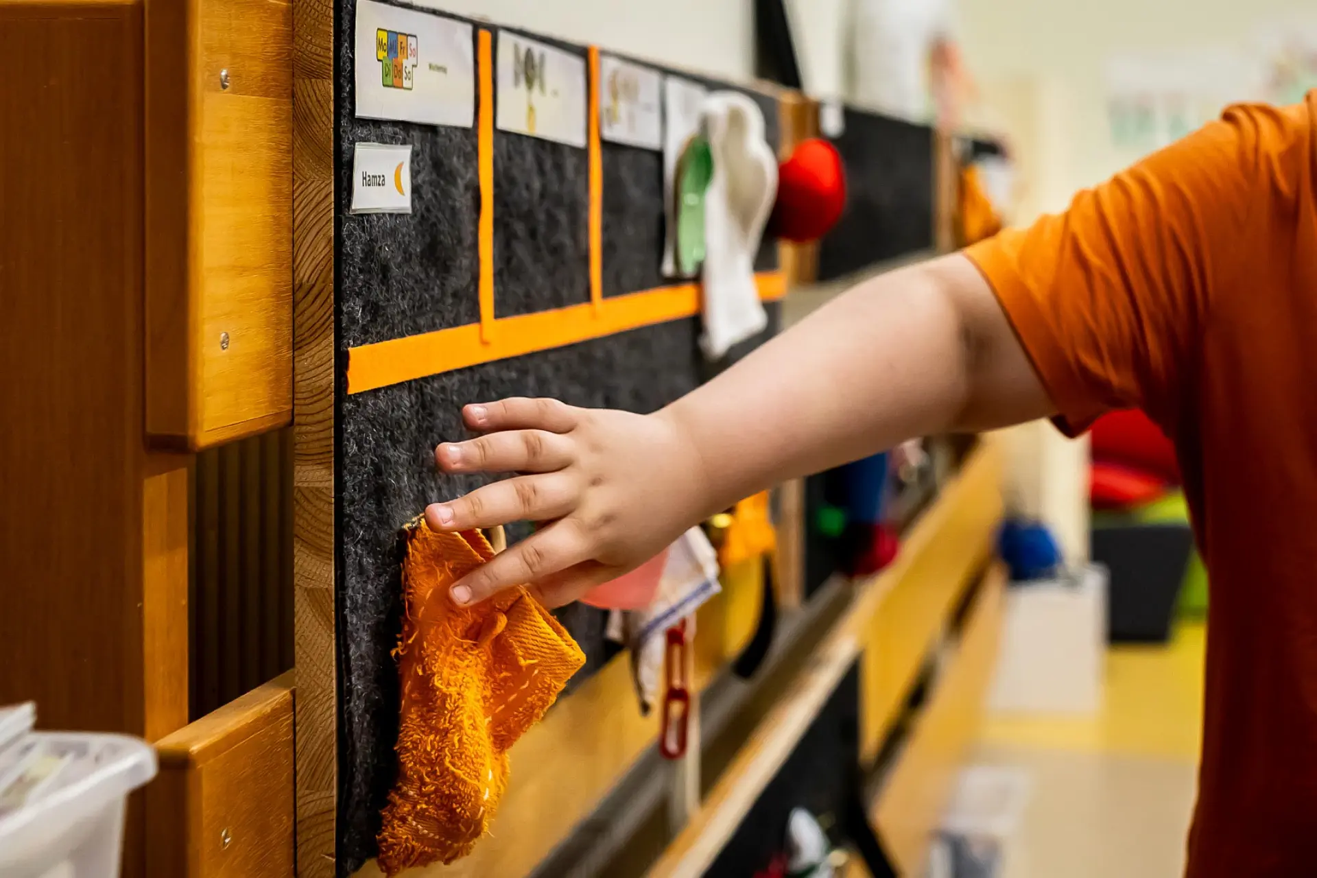 Ein Schulkind geht mit seinen Fingern über einen taktilen Stundenplan. Der Plan ist an der Wand in einem Klassenzimmer angebracht.